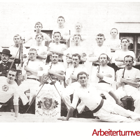 Gruppenfoto von Männern in weißer Sportkleidung, die 1912 im Arbeiterturnverein posieren, umgeben von Turngeräten.