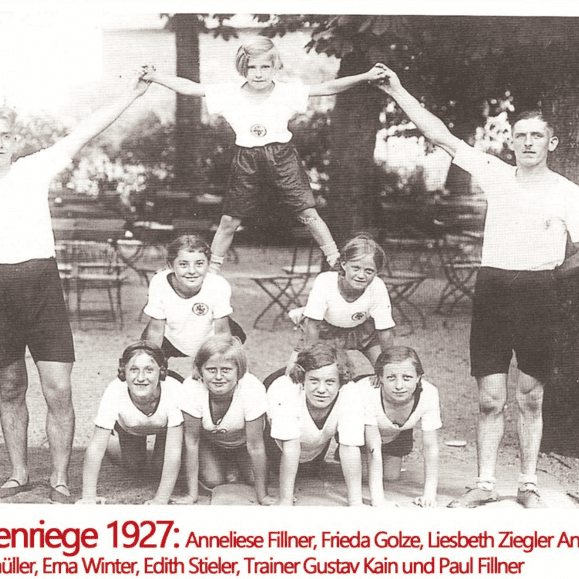 Gruppenaufnahme von Mädchen im Sportoutfit 1927, die eine Menschenpyramide bilden, mit zwei Männern als Trainer.