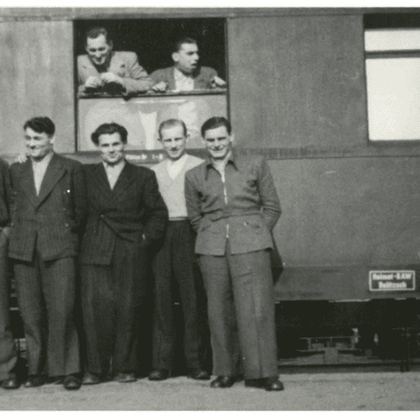 Gruppierung von acht Männern vor einem Zug, einige schauen aus einem Fenster, Aufnahme aus Chemnitz 1954.