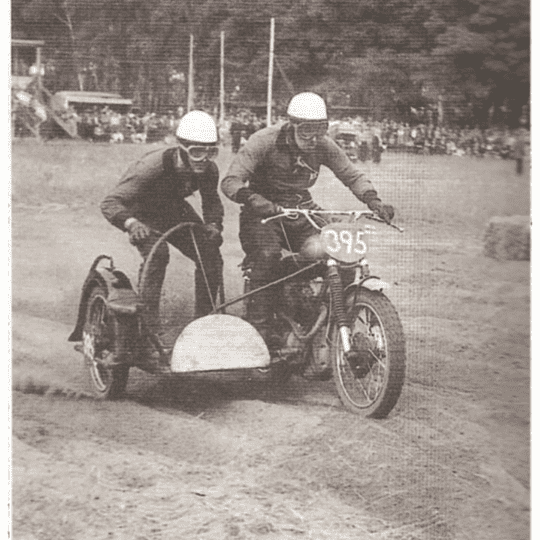 Motorradgespann beim Motocross-Rennen 1960 mit zwei Fahrern, einer davon hält den Lenker.