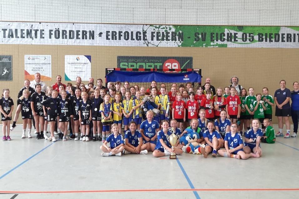 Gruppenfoto von M&auml;dchenmannschaften in Sportkleidung, versammelt vor einem Banner in einer Sporthalle.