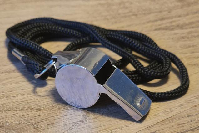 Silberner Metallpfeife mit schwarzem Band liegt auf einer Holzoberfl&auml;che.