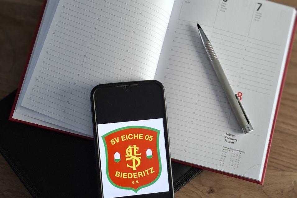 Smartphone mit Vereinslogo &bdquo;SV Eiche 05 Biederitz&ldquo; liegt auf einem ge&ouml;ffneten Terminplaner und einem Silberstift.