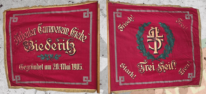 Rote Vereinsfahne mit goldener Schrift, Wappen und Ornamenten, Schriftzug „Biederitz“ und Gründungsdatum 21. Mai 1915.