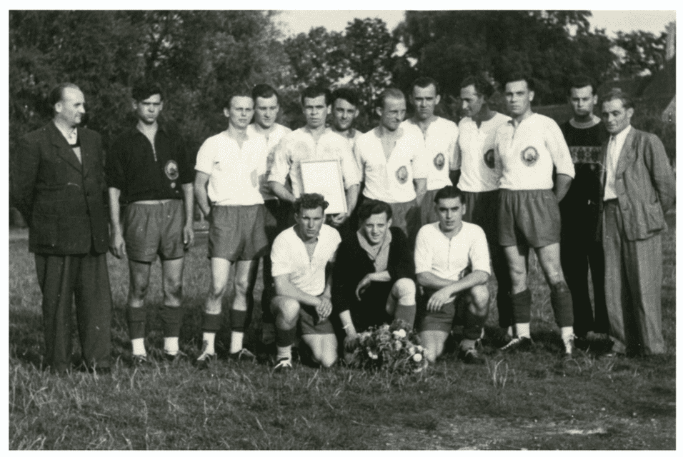Mannschaftsfoto einer Fu&szlig;ballmannschaft mit Pokal, umgeben von 13 Spielern und 3 Trainern im Freien.