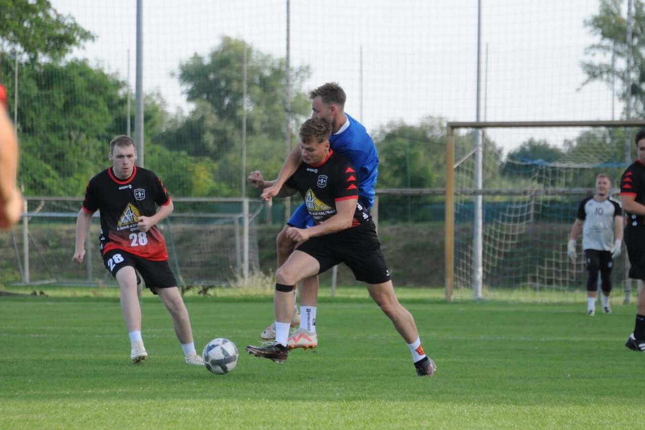 Gruppen von Fußballspielern auf einem Rasenfeld, ein Spieler wird von hinten am Ball gehindert.