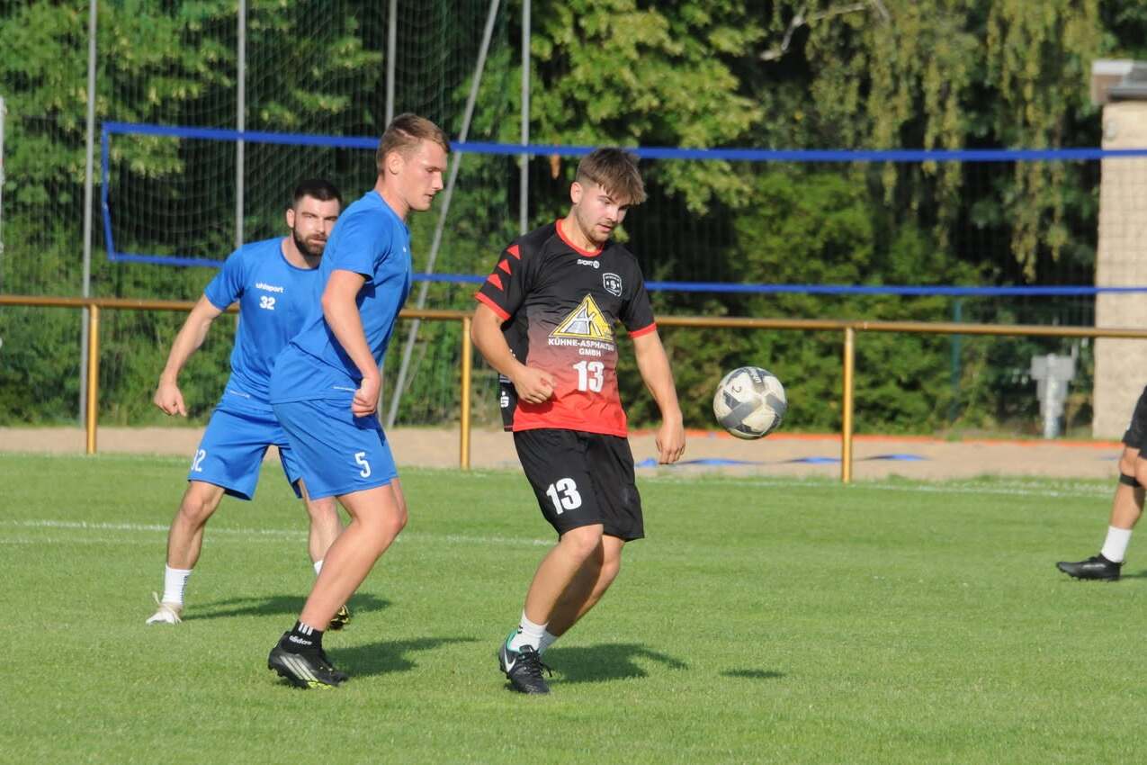 Zwei Fußballspieler in Aktion auf dem Spielfeld, ein Spieler mit Ball, der andere in blauer Uniform.