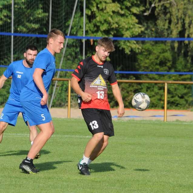 Zwei Fußballspieler in Aktion auf dem Spielfeld, ein Spieler mit Ball, der andere in blauer Uniform.