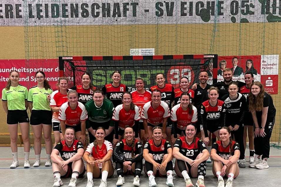 Gruppenfoto einer Handballmannschaft mit Trainer, in Sportkleidung und vor einem Handballtor stehend.