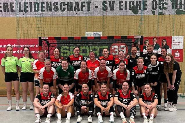 Gruppenfoto einer Handballmannschaft mit Trainer, in Sportkleidung und vor einem Handballtor stehend.