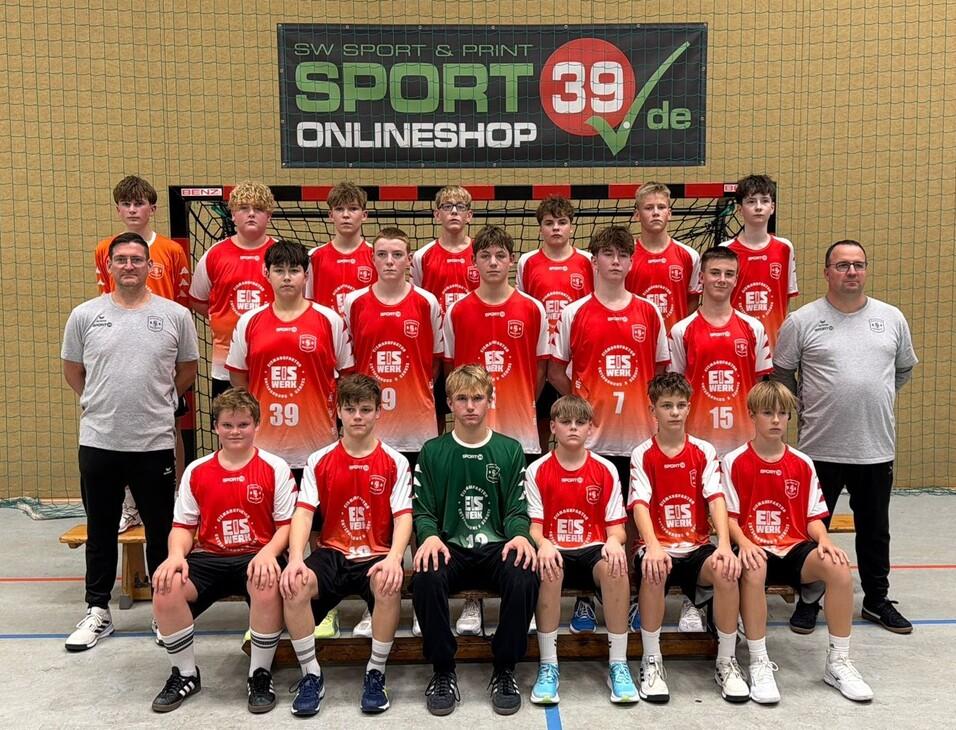Mannschaftsfoto einer Jugend-Handballmannschaft in roten Trikots vor einem Handballtor in einer Sporthalle.