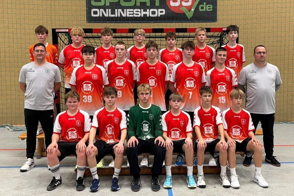 Mannschaftsfoto einer Jugend-Handballmannschaft in roten Trikots vor einem Handballtor in einer Sporthalle.