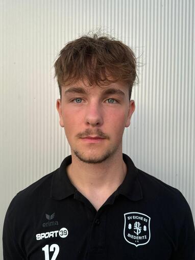 Portrait eines jungen Mannes mit kurzem Haar, in einem schwarzen Fu&szlig;balltrikot mit der Nummer 12.