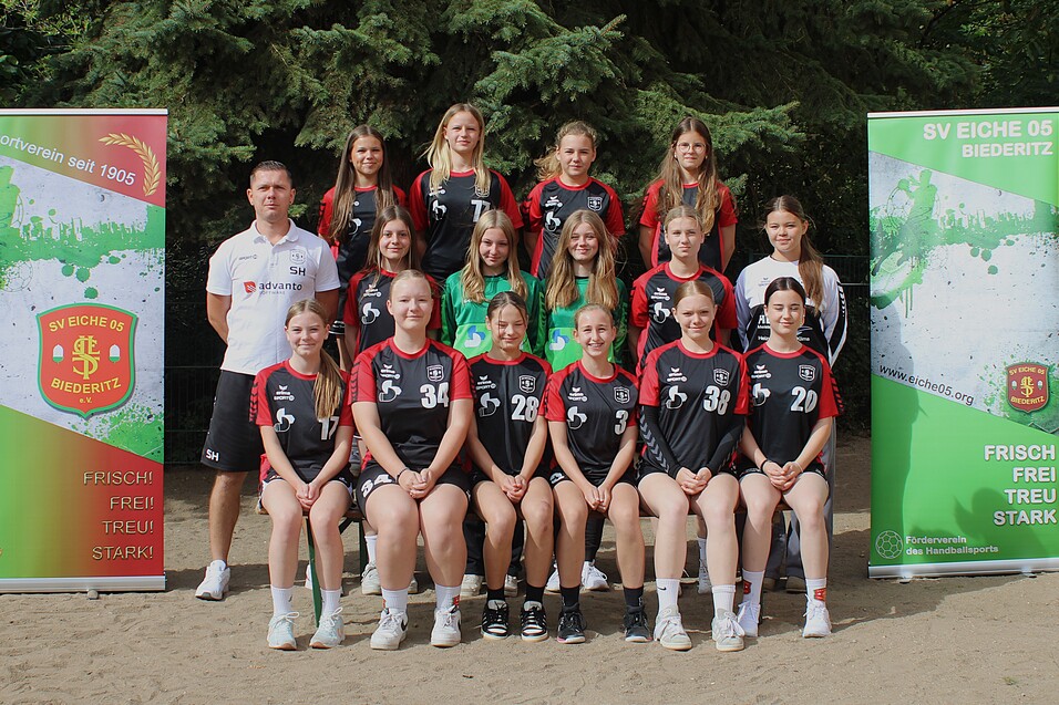 Teamfoto der weiblichen Handballmannschaft SV Eiche 05 Biederitz mit Trainer, umgeben von Banner mit Vereinslogo.