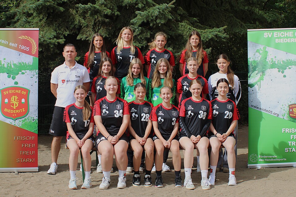 Teamfoto der weiblichen Handballmannschaft SV Eiche 05 Biederitz mit Trainer, umgeben von Banner mit Vereinslogo.
