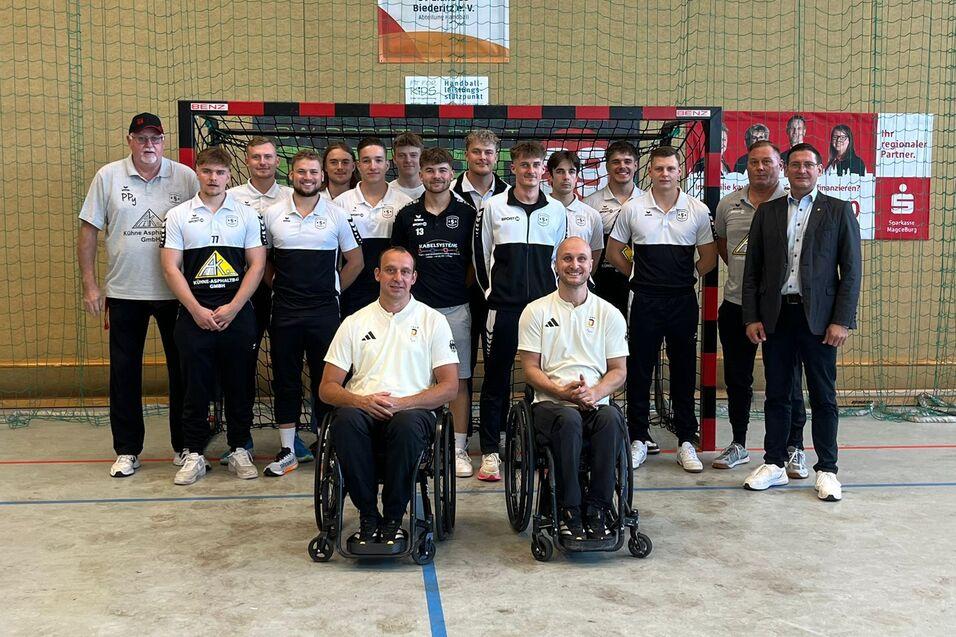 Gruppenfoto von Spielern in Sportkleidung vor einem Handballtor, darunter zwei Rollstuhlfahrer und Trainer.