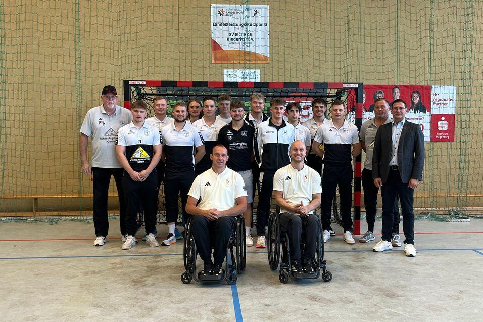 Gruppenfoto von Spielern in Sportkleidung vor einem Handballtor, darunter zwei Rollstuhlfahrer und Trainer.