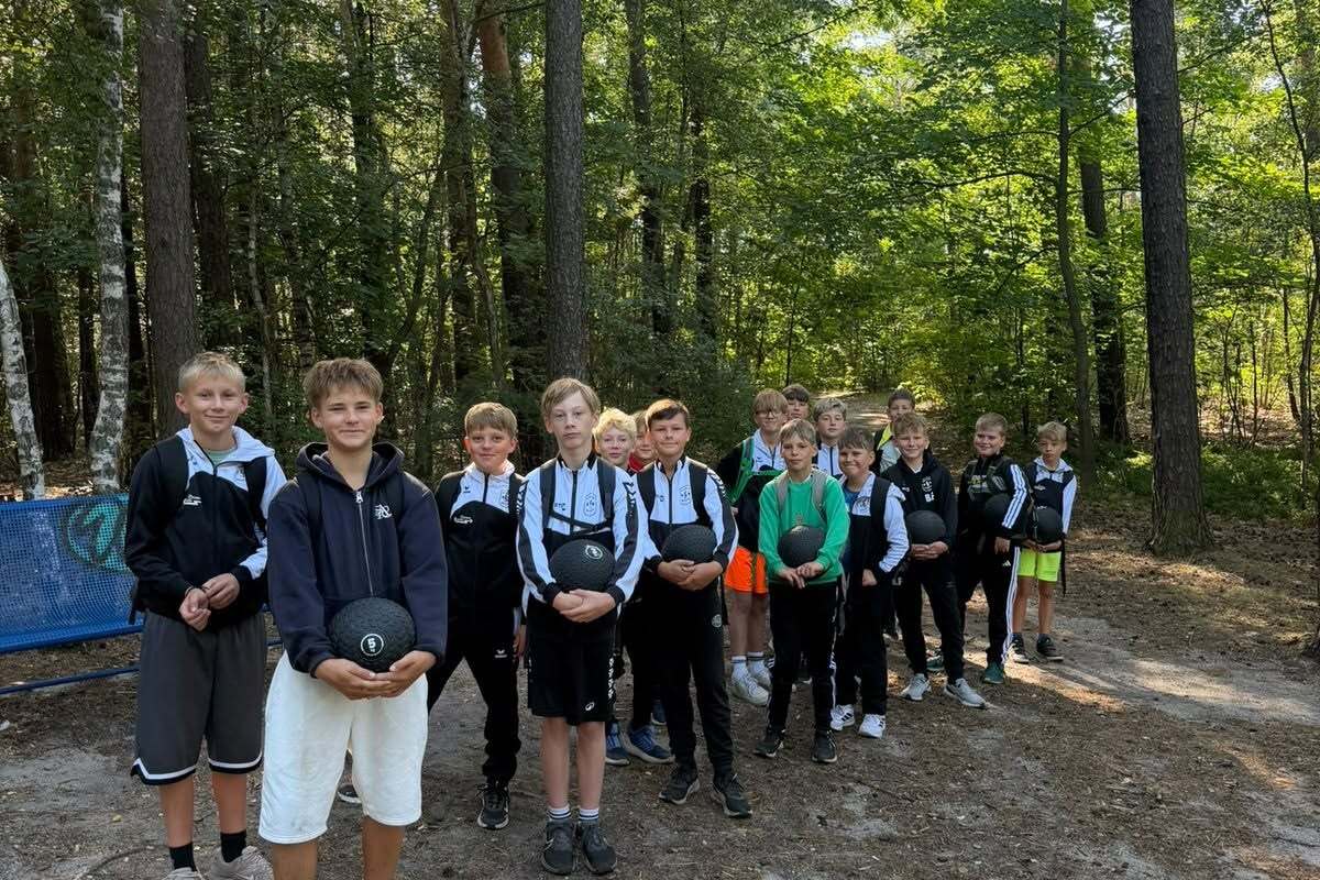 Gruppe von Jungen im Wald, die zusammen mit Sportbällen auf einem sandigen Pfad stehen.
