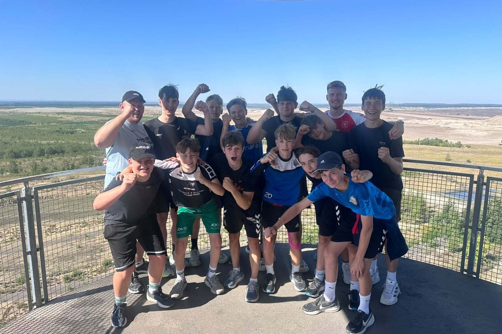 Gruppe von Jugendlichen posiert freudig auf Aussichtsplattform mit Blick auf Landschaft und Himmel.