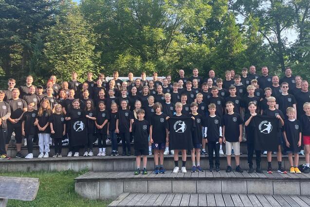Gruppenfoto von &uuml;ber 100 Teilnehmern in schwarzen T-Shirts, auf Treppenstufen vor B&auml;umen und einem Geb&auml;ude.
