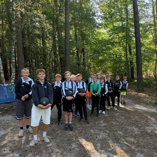 Gruppe von Jungen im Wald, die zusammen mit Sportbällen auf einem sandigen Pfad stehen.