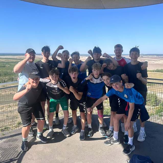 Gruppe von Jugendlichen posiert freudig auf Aussichtsplattform mit Blick auf Landschaft und Himmel.