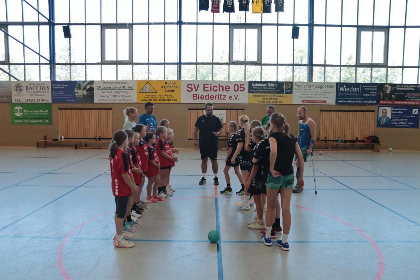 Zwei Gruppen von Mädchen im Sportdress stehen sich in einer Halle gegenüber, bereit für ein Handballspiel.