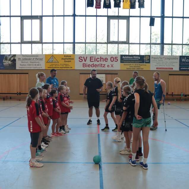 Zwei Gruppen von Mädchen im Sportdress stehen sich in einer Halle gegenüber, bereit für ein Handballspiel.