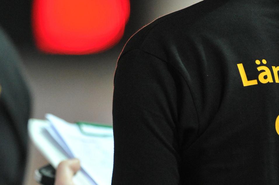 Person in schwarzem T-Shirt hält ein Notizbuch und Stift, im Hintergrund leuchtende Ampeln.